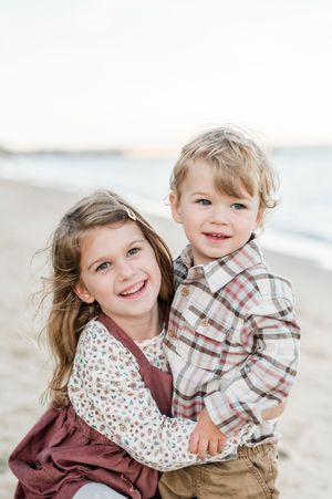Two children in coordinating outfits share sweet moments together on a beach during a photo session.