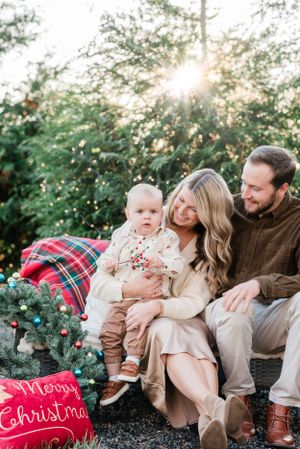 Holiday family photo with Christmas decorations and sunset through evergreen trees.