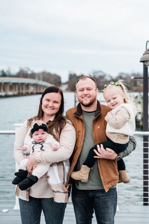 Happy young family with two small children posing on a waterfront dock on a cloudy winter day.