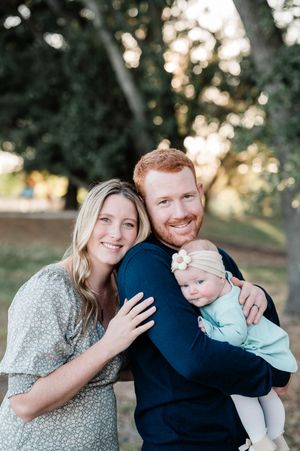 Smiling couple holding a baby girl in a park during golden hour family portrait session.