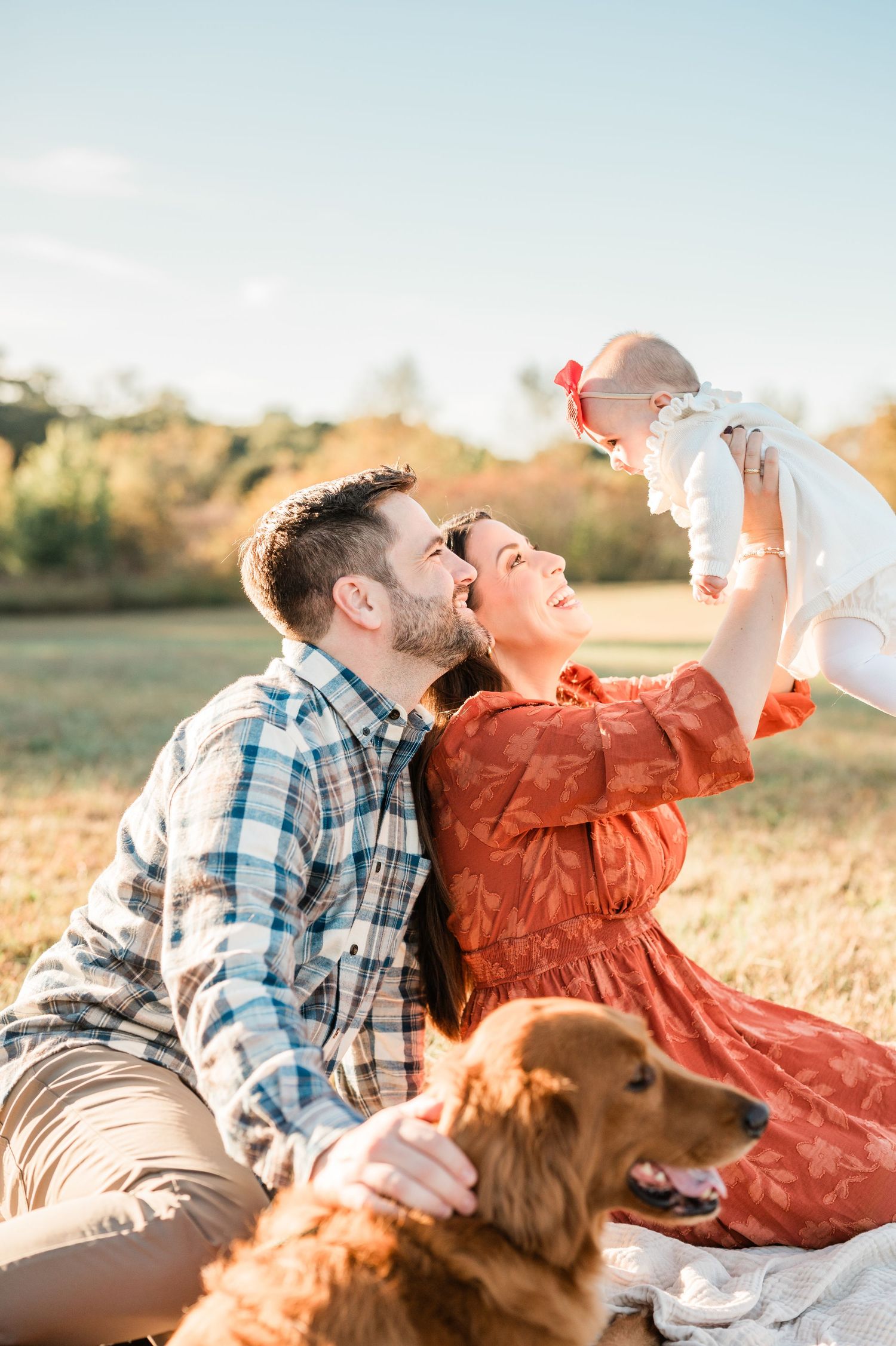 A couple and their golden retriever dog lay in a grassy field at sunset blowing bubbles together.