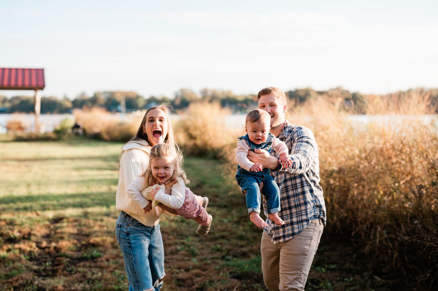Happy family with two young children playing outdoors in a scenic field during a warm autumn day.