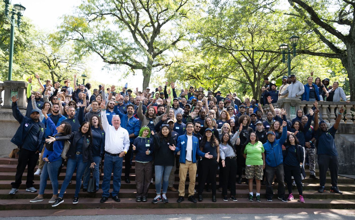 Large group of people gathered outdoors under trees for a community event.