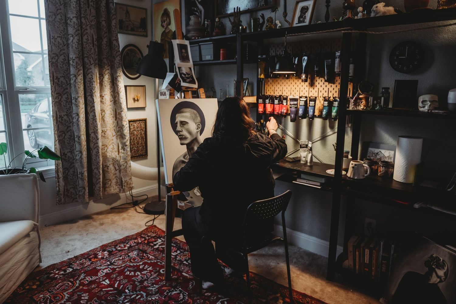Dark silhouette sits in a vintage room filled with instruments, artwork and a red Persian rug by a window.