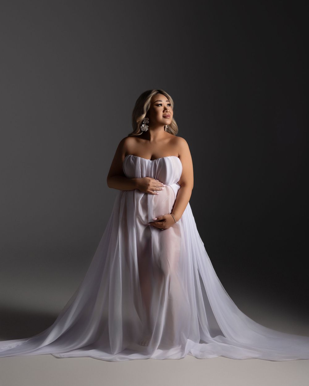 A graceful figure in a flowing lilac gown and sheer cape poses elegantly against a dark grey studio backdrop.