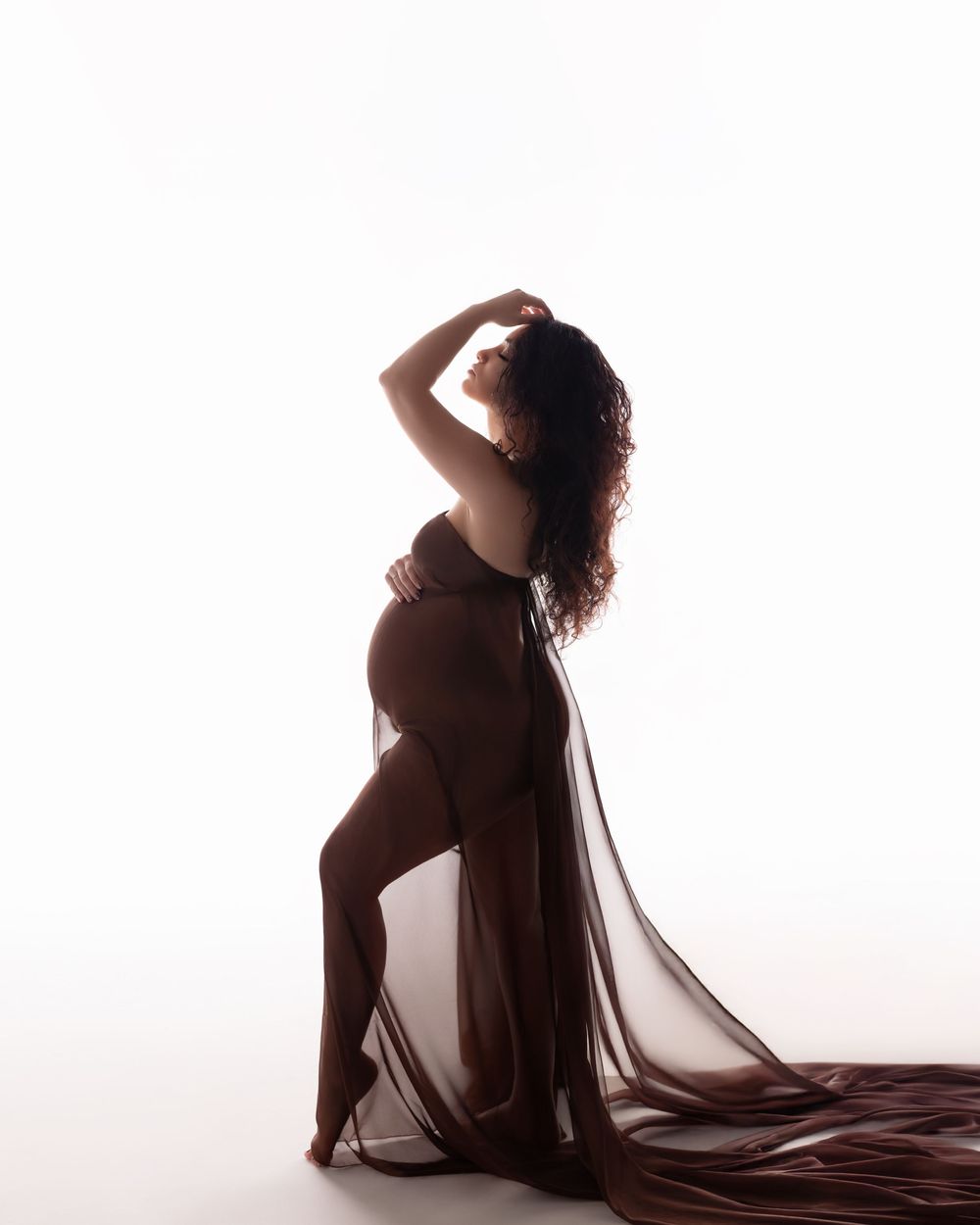 Artistic silhouette series showing four poses of a pregnant woman in flowing fabric against a bright white backdrop.