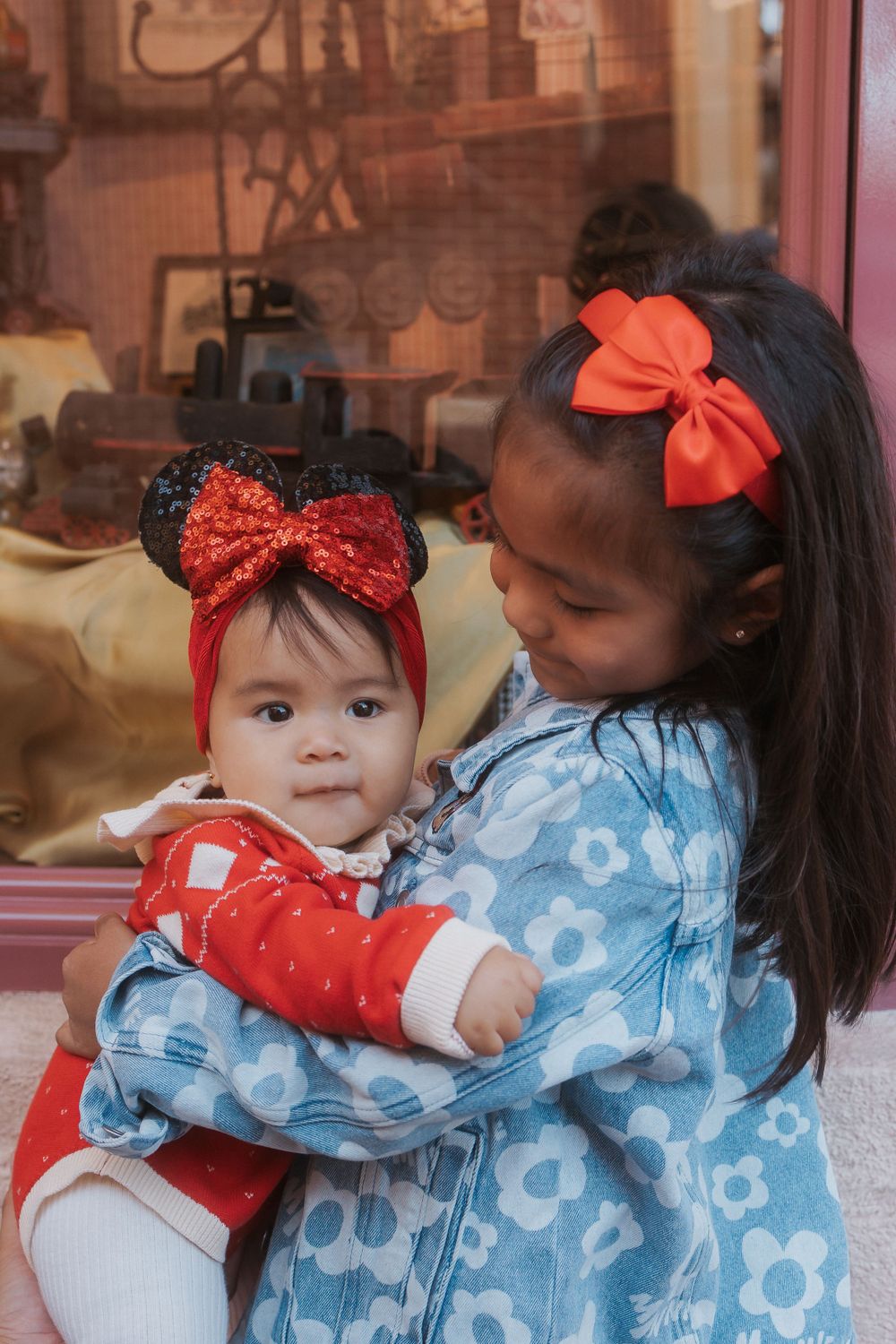 Two children in coordinating Disney outfits share a sweet hug by store window.