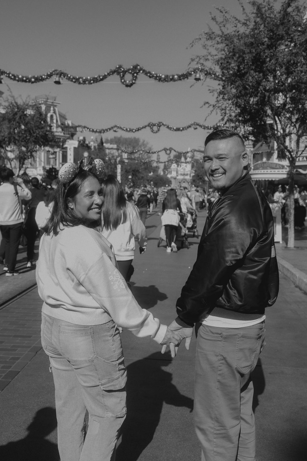 A couple holds hands while walking down Main Street at Disney theme park with festive garland overhead.