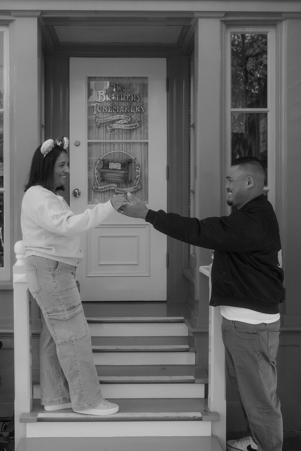 A playful couple poses on white porch steps in front of a classic door.
