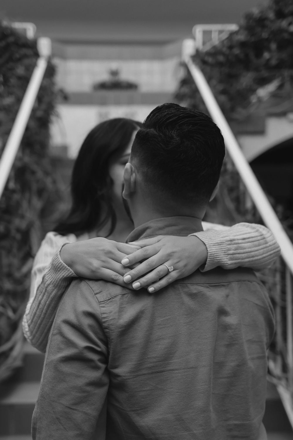 A couple embraces on a staircase with white railings in an intimate black and white portrait.