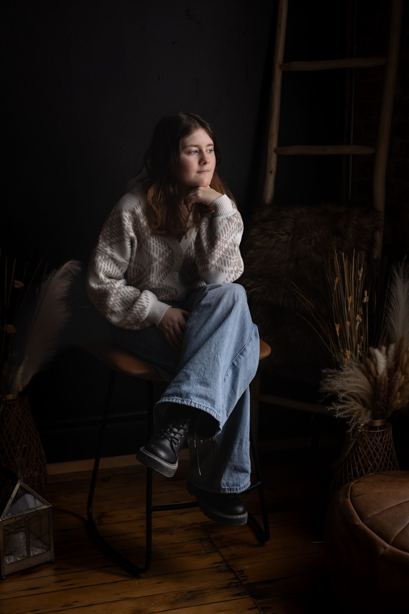 A person in a cozy sweater sits thoughtfully in a dark room with dramatic lighting.