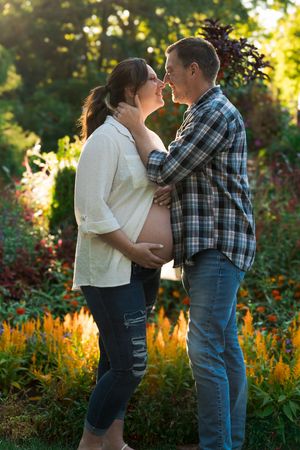 A couple shares an intimate moment in a garden at sunset while expecting a baby.
