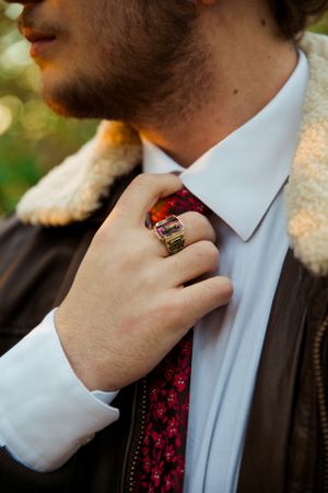Close-up of formal attire with red patterned tie and ring detail.