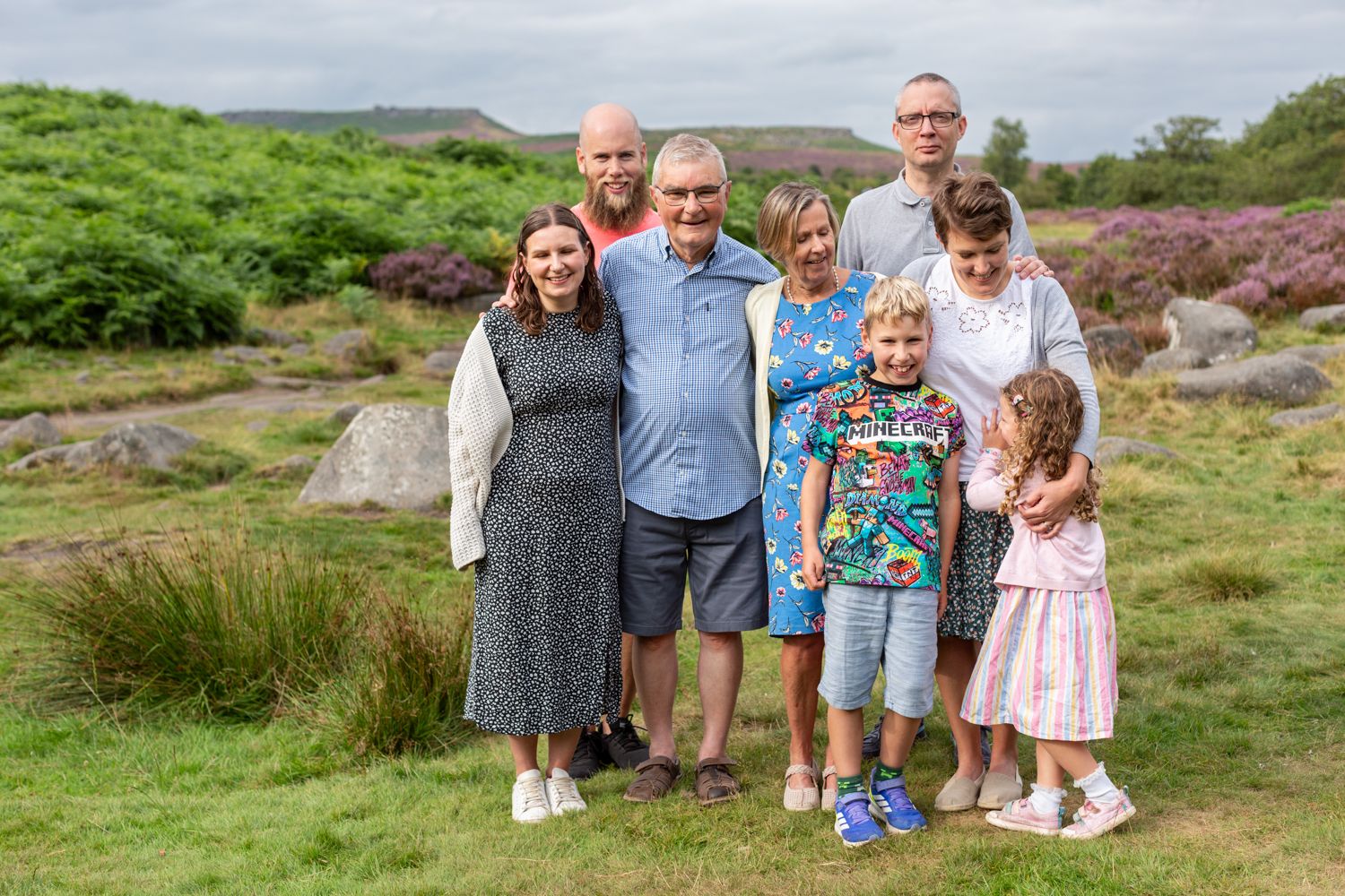 Family enjoying time together outdoors on a hillside with blooming heather and green fields.