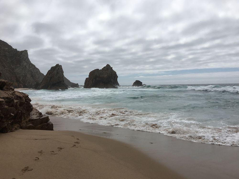 Sea and large rocks standing in the water. dramaic clounds. foot steps in sand.