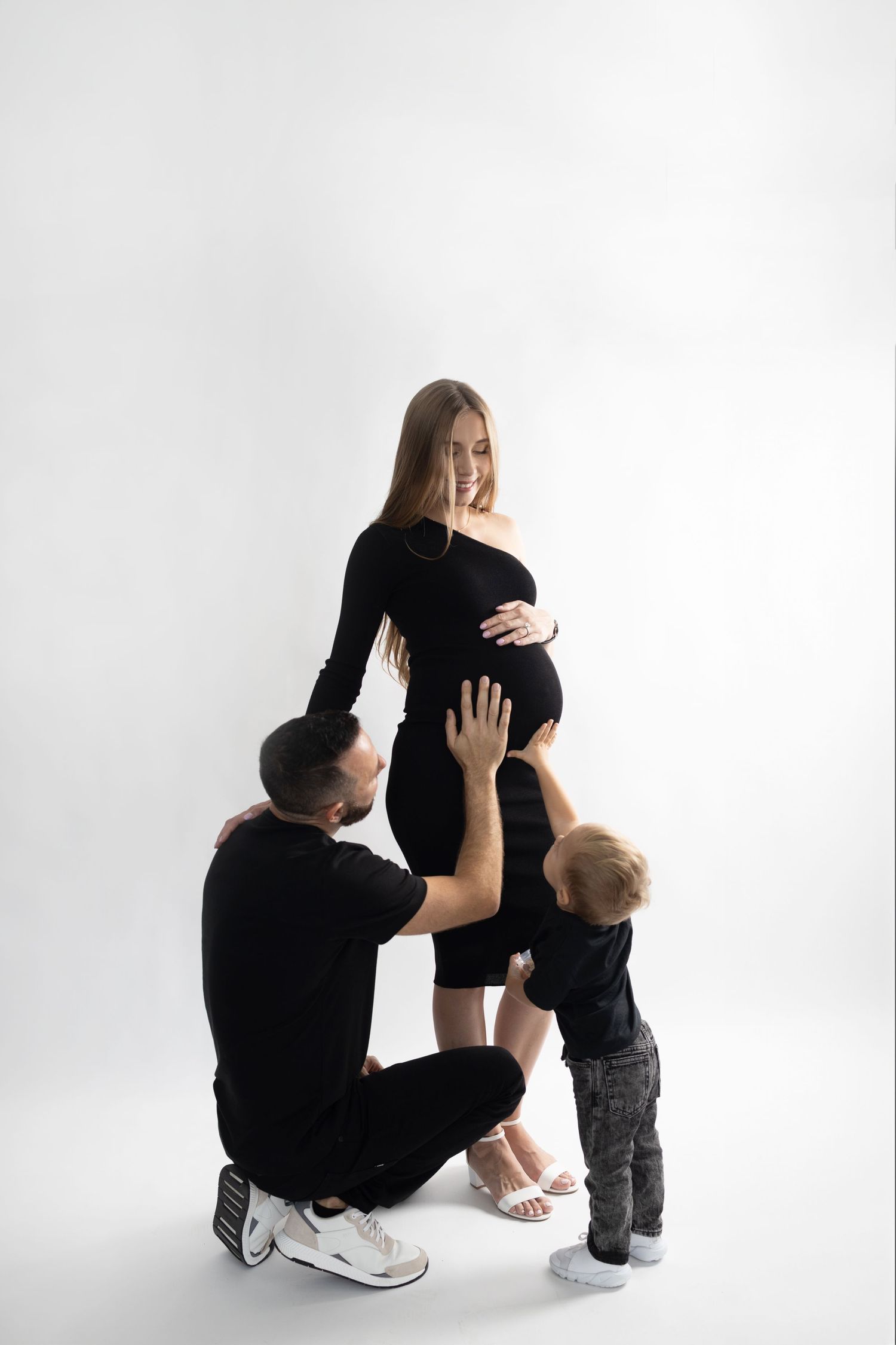 Professional maternity photo shoot showing an intimate family moment against a white backdrop.