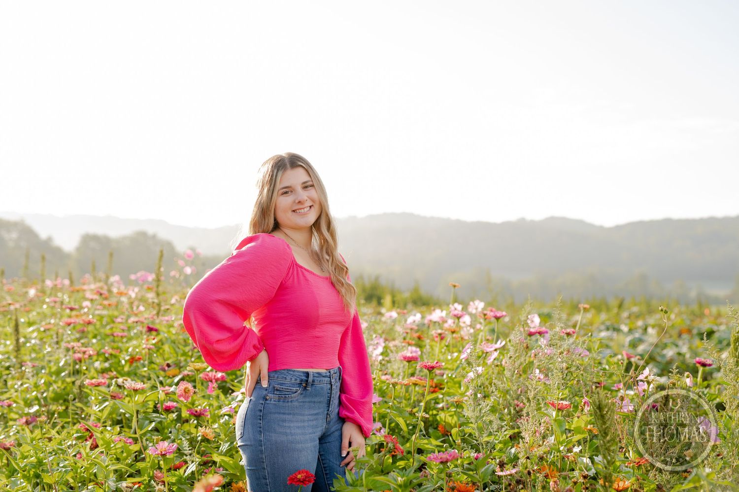 Someone poses in a vibrant pink sweater among wildflowers in a scenic mountain field.