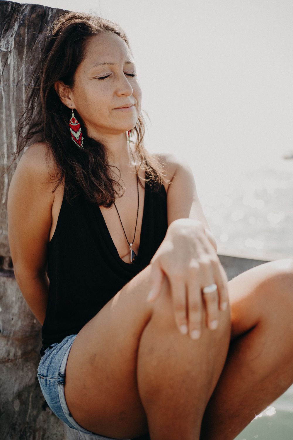 A woman in casual beachwear relaxes against a wooden post near the ocean photoshoot in Puerto Morelos.