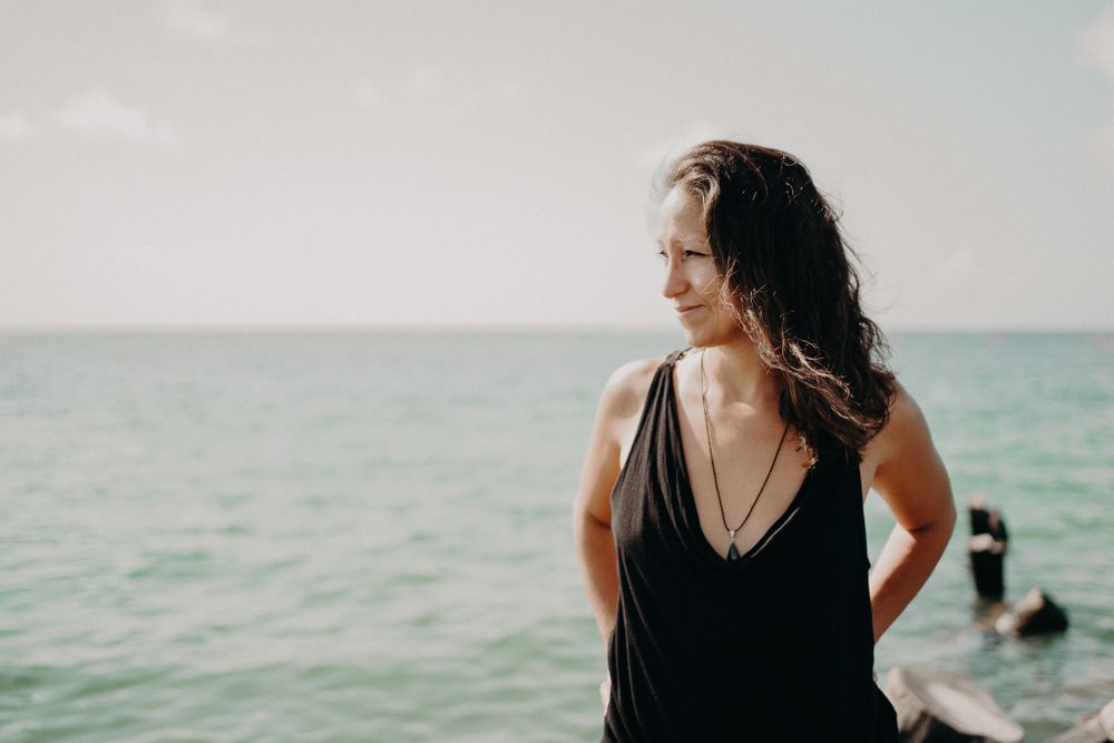 A woman in a black top stands by the ocean on a bright sunny day photoshoot in Puerto Morelos.