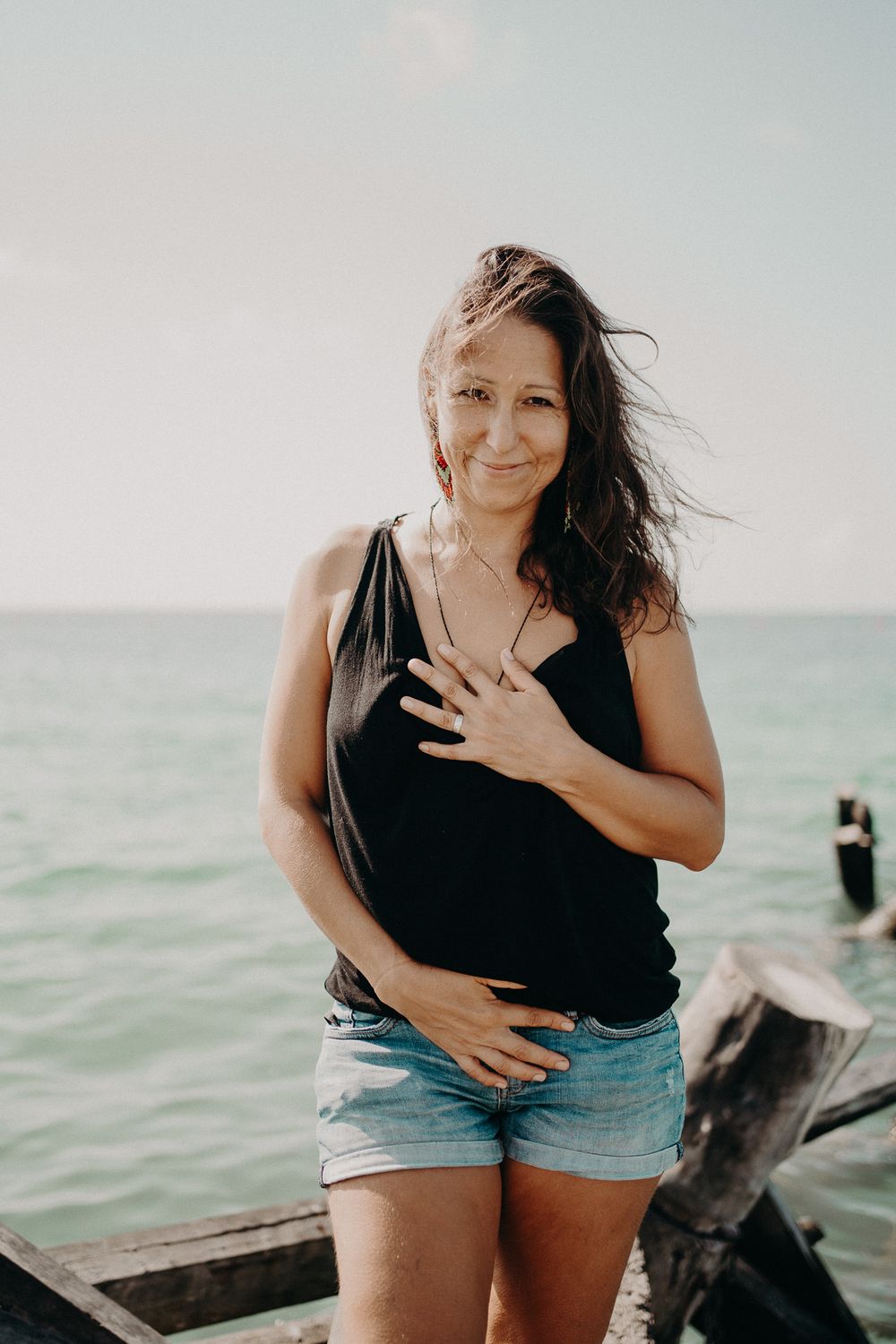 A woman in casual summer attire smiles while standing near the ocean photoshoot in Puerto Morelos.