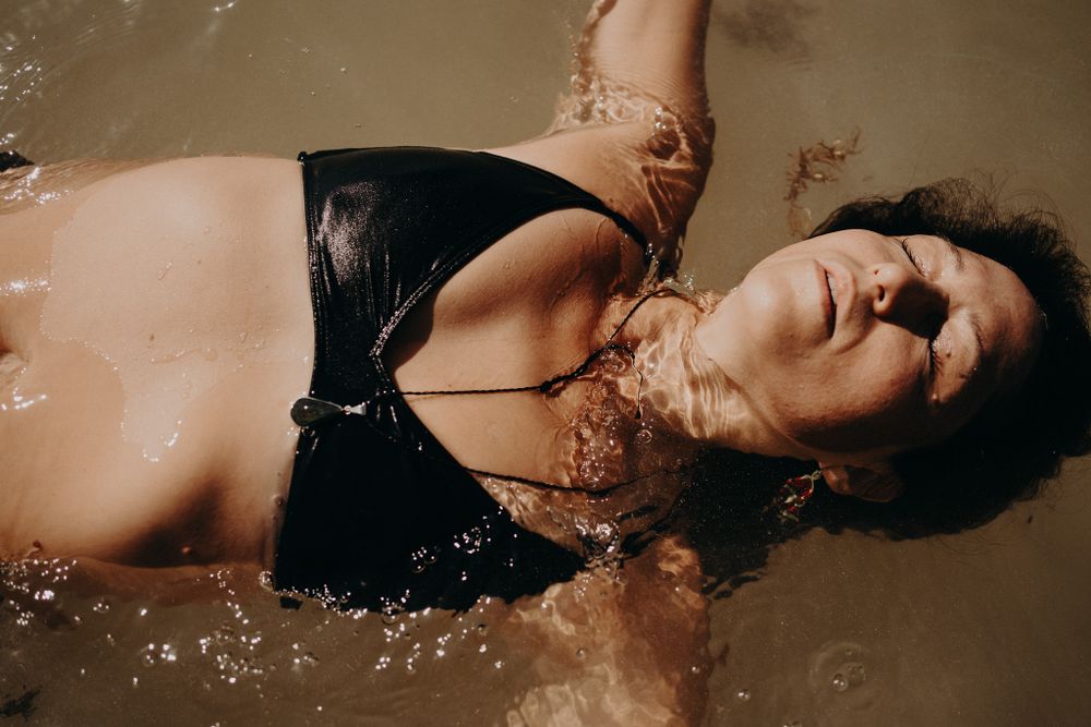 A candid artistic shot of someone in black swimwear floating in murky water photoshoot in Puerto Morelos.