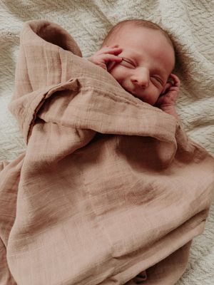 A sleeping newborn wrapped in soft beige linen fabric.