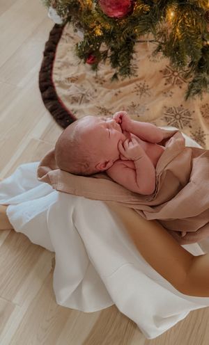 Newborn baby sleeping peacefully under Christmas greenery decoration.