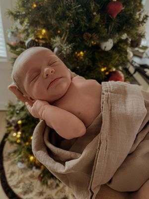 A sleeping newborn baby in beige swaddle cloth with Christmas decorations in background.