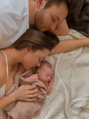 A tender family moment with a newborn baby resting between parents on white bedding.