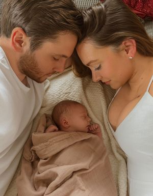 Parents gazing lovingly at their newborn baby wrapped in beige fabric.