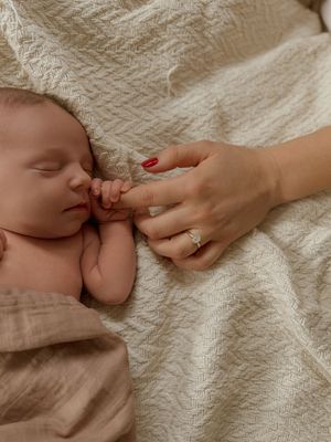 Gentle hands caressing a newborn baby on textured white bedding.