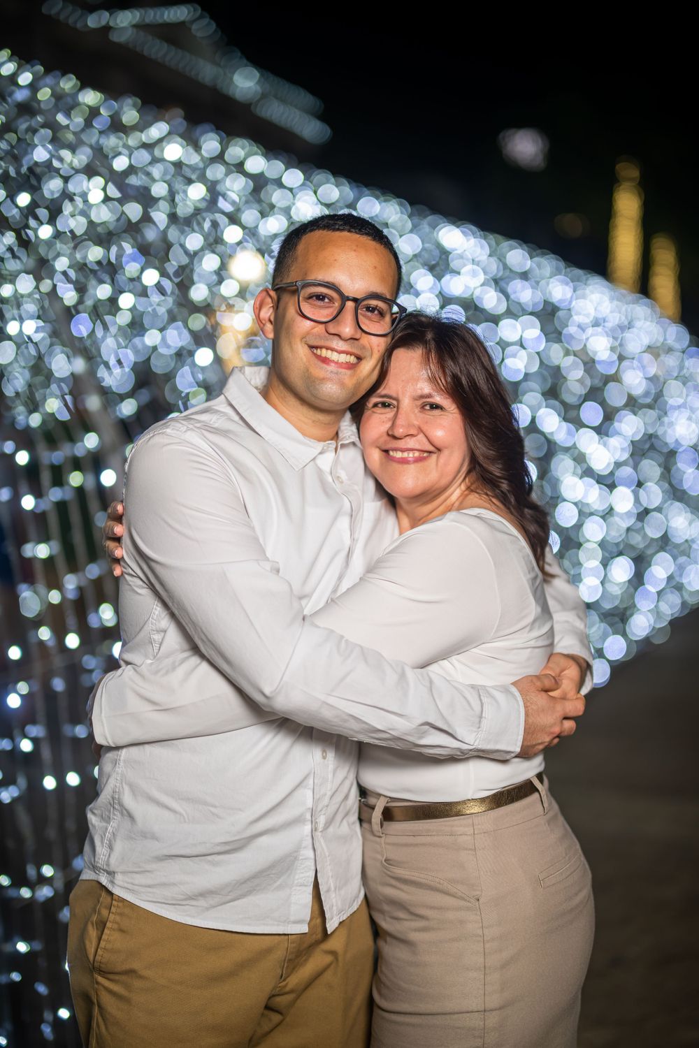 Couple embracing in front of twinkling light display at night.