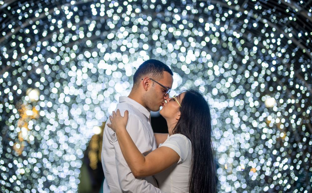 Romantic couple embracing in front of cascading white lights at night.