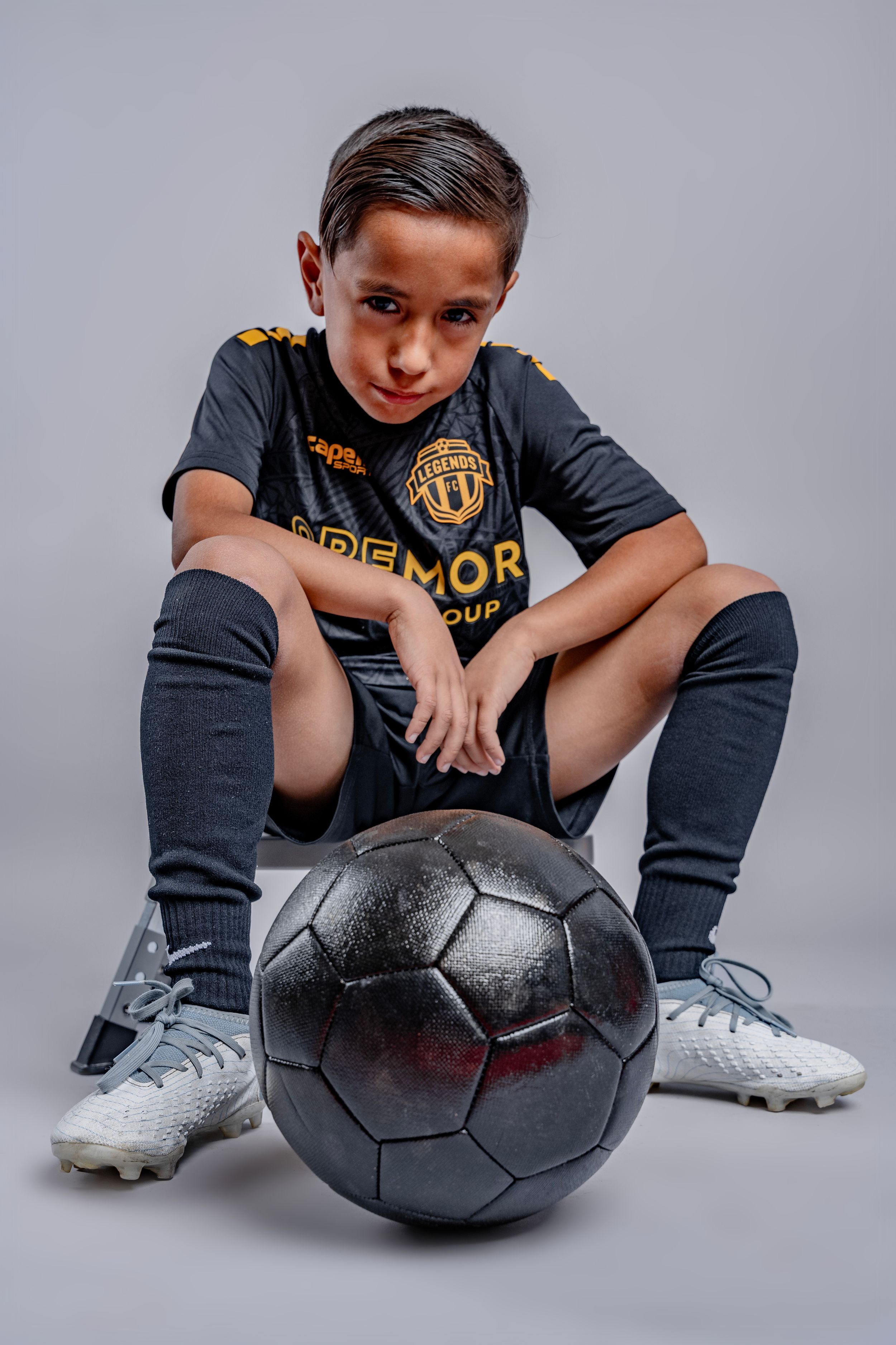 Soccer player in black uniform poses with ball in professional studio setting.