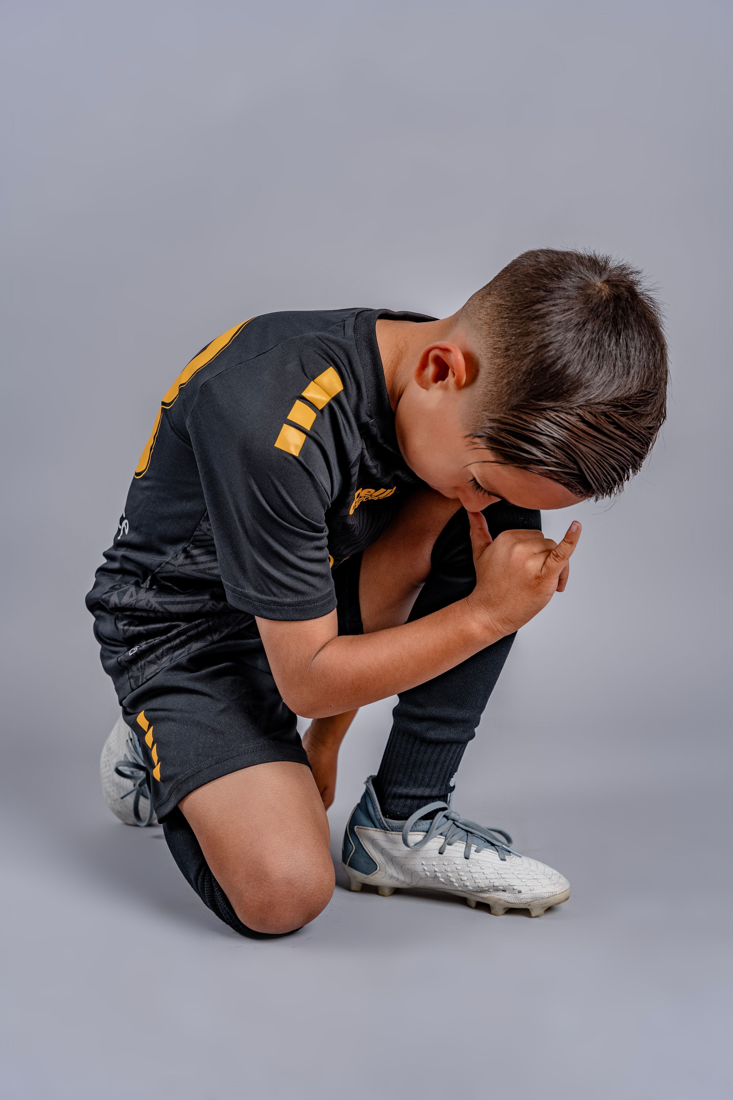 Soccer player in black uniform kneels dramatically during studio photoshoot.