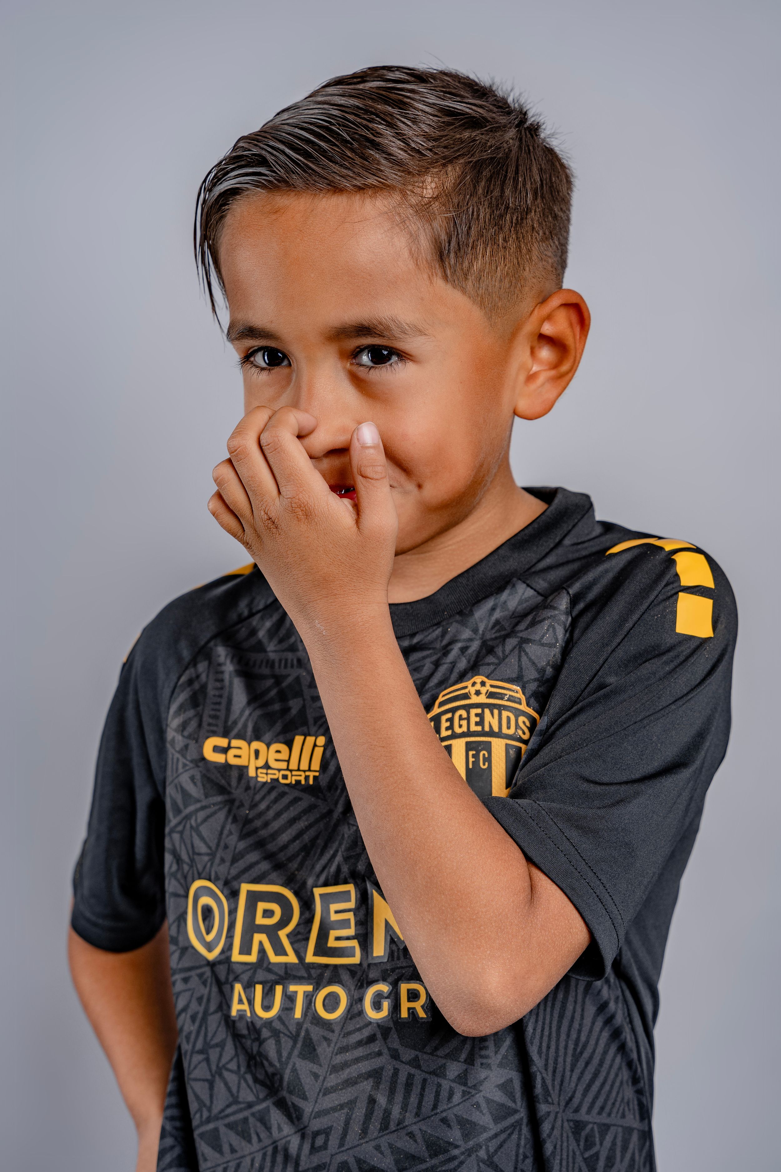 Athlete in black Legends FC jersey covers face playfully during photo shoot.
