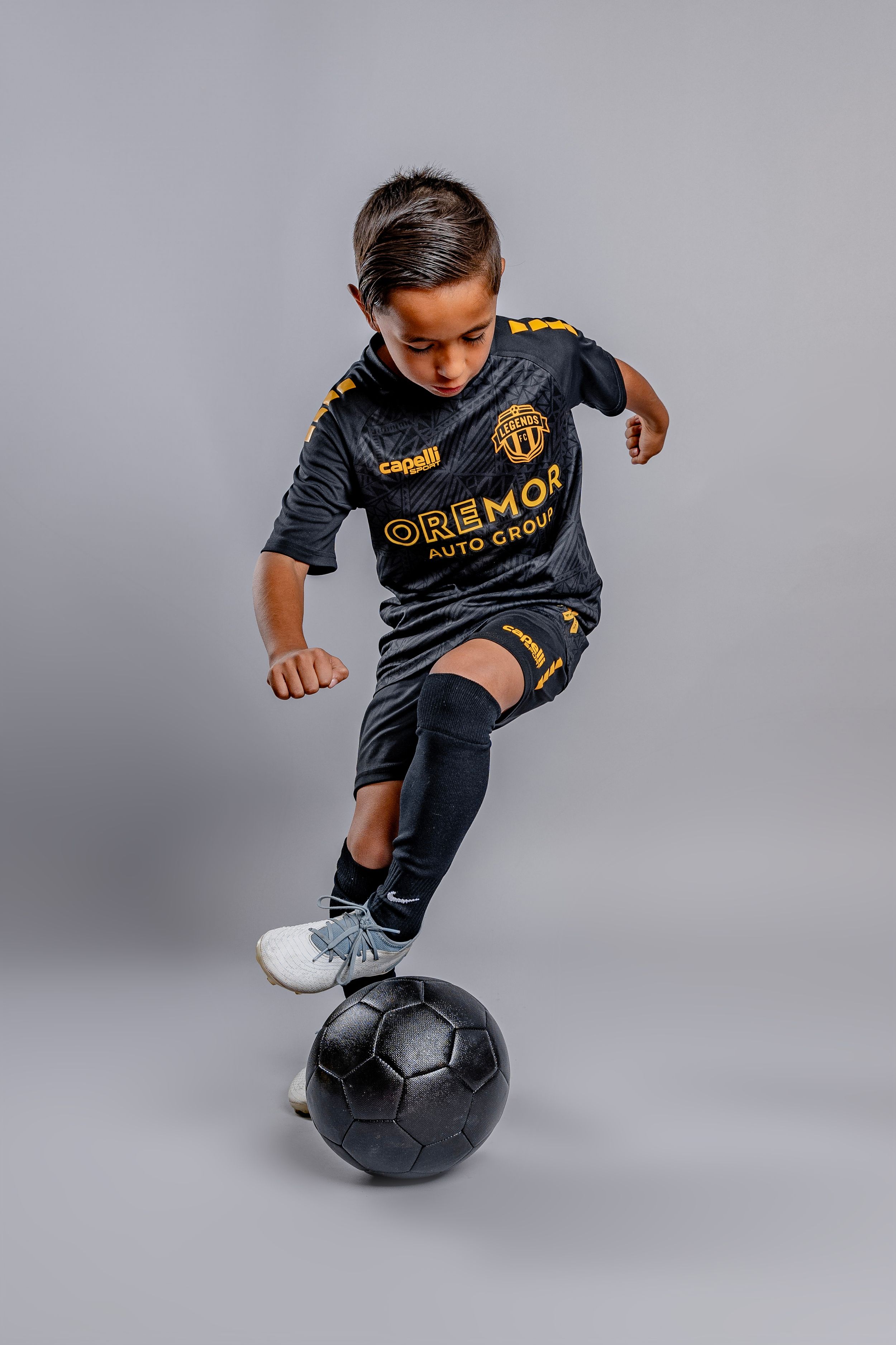 Soccer player in black uniform demonstrates ball control skills against grey background.
