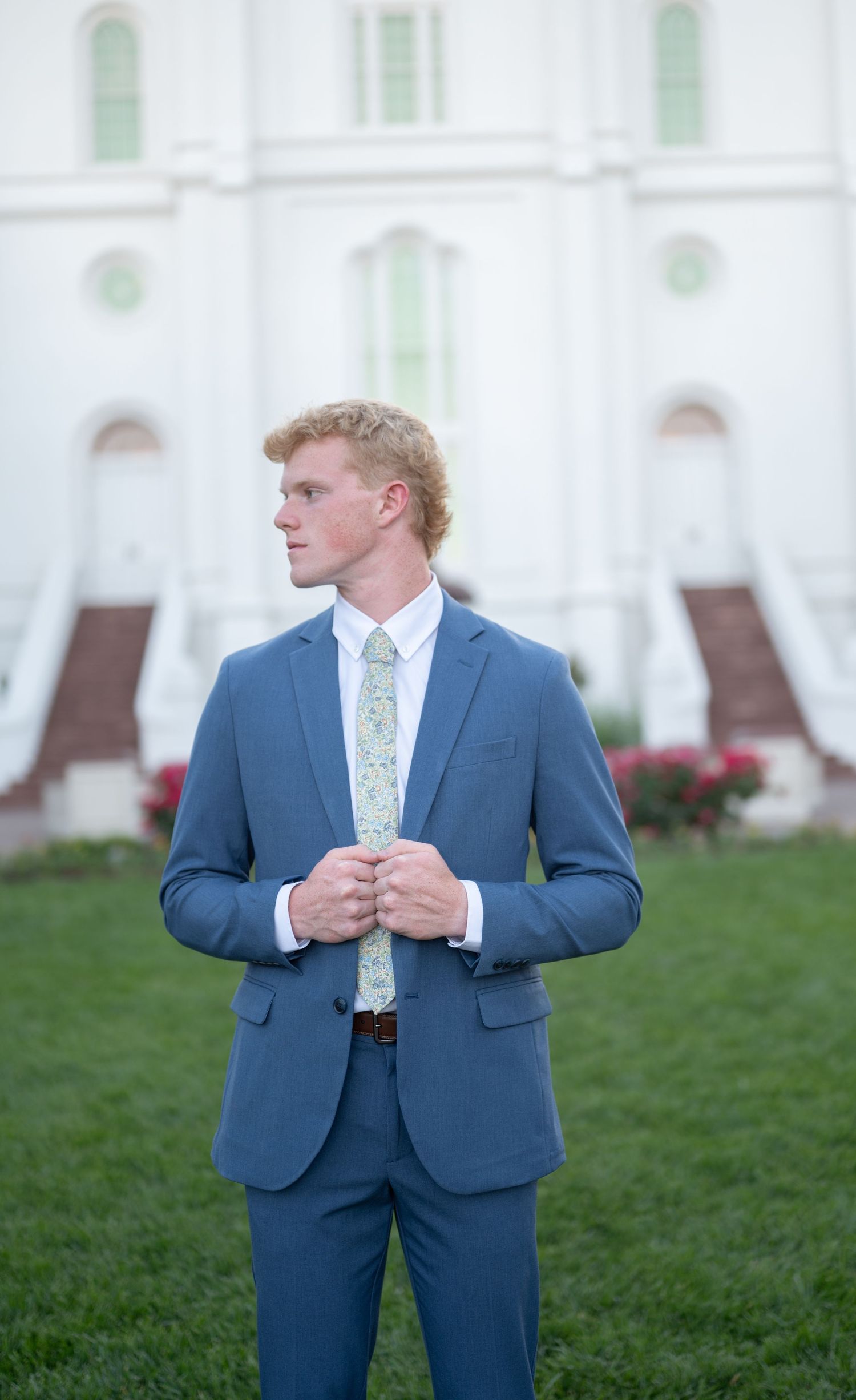 A person in a blue suit stands in front of a white church building with green accents.