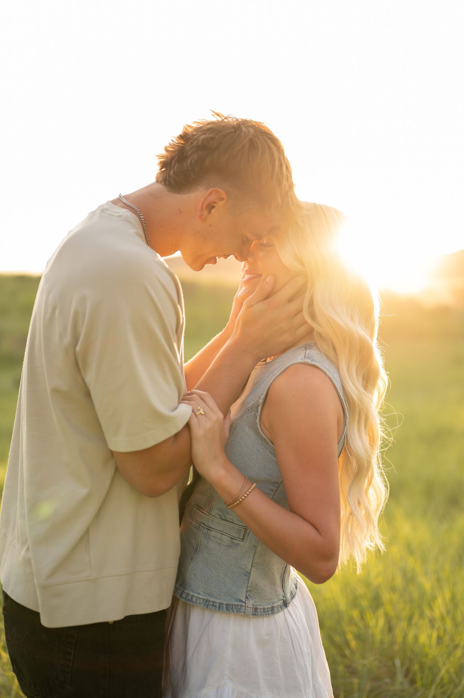 A tender embrace between two people in a sunlit field at golden hour.