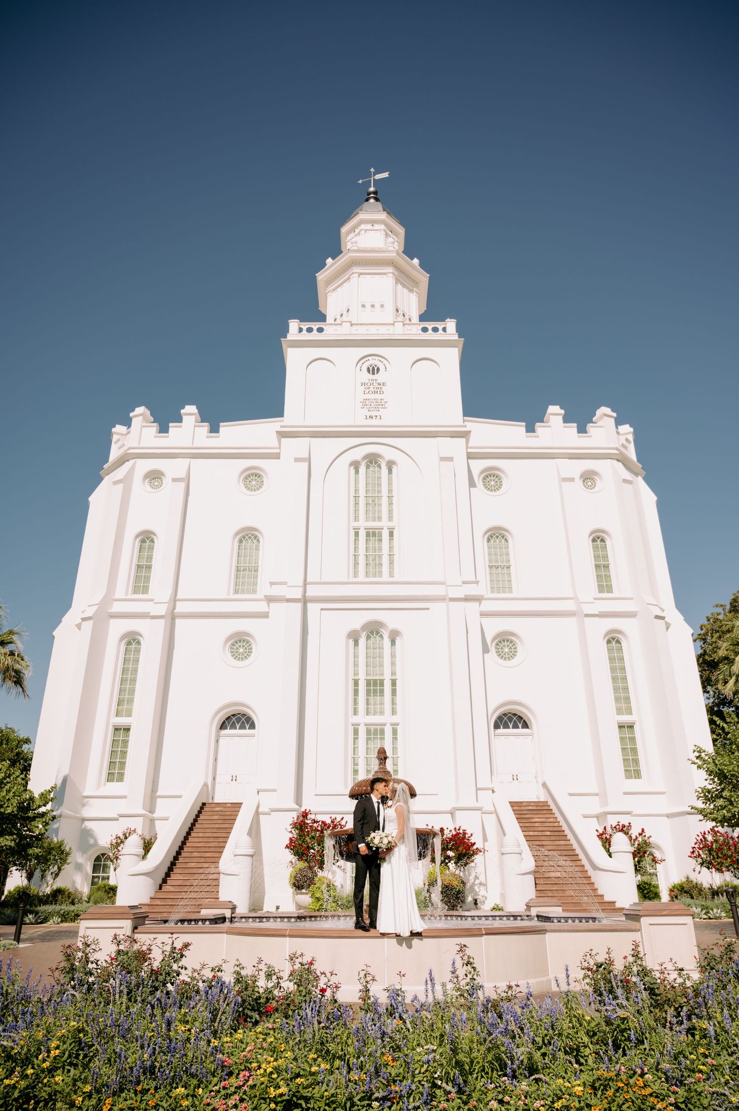 A wedding couple poses in front of the grand white St. George Utah Temple.