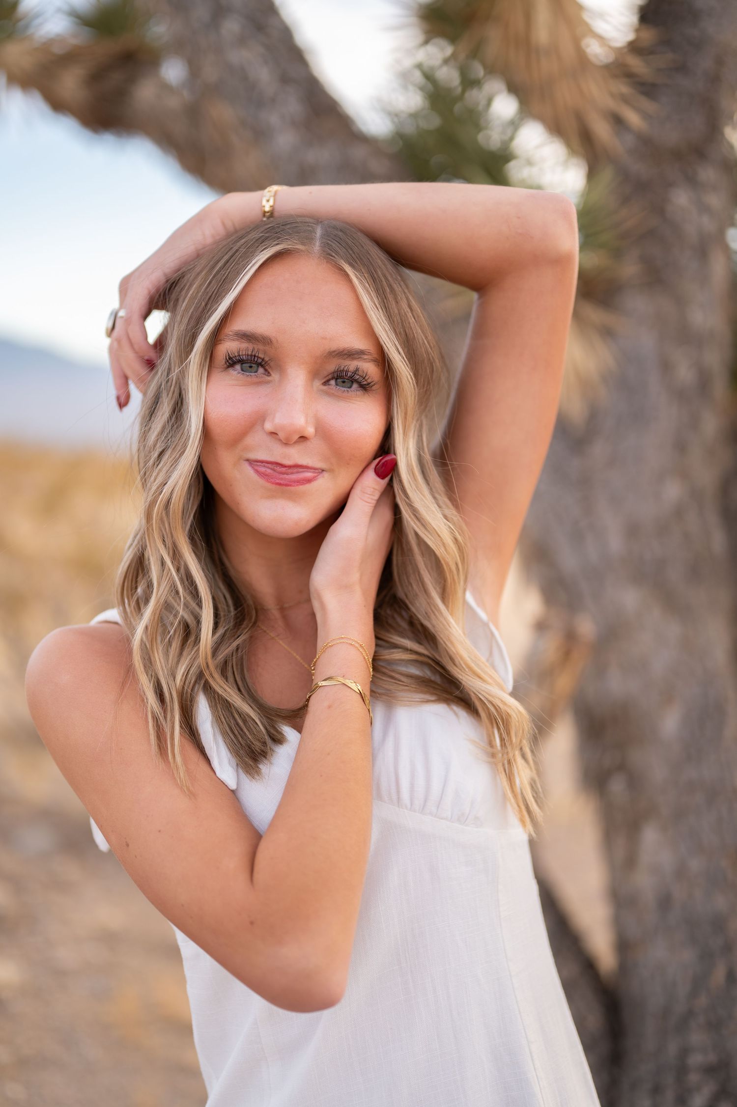 A portrait of someone in a white top posing outdoors with natural lighting.