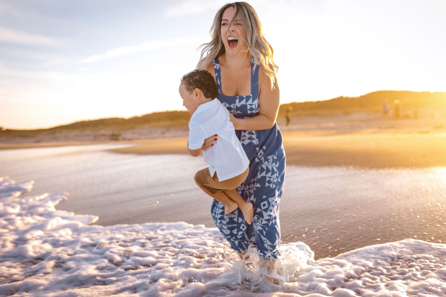 A woman in blue patterned workout wear splashes through shallow water on a beach at sunset.