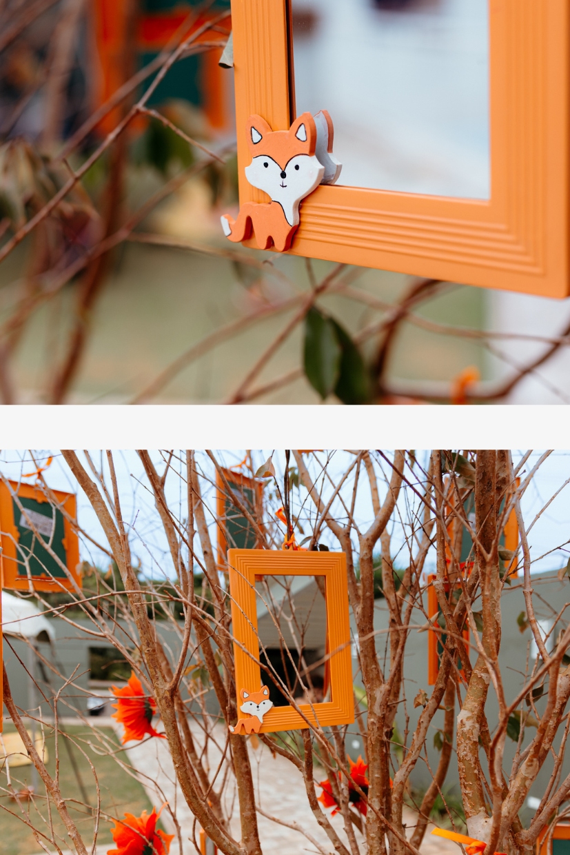 Orange picture frames with fox decorations hang among bare tree branches creating a whimsical outdoor display.