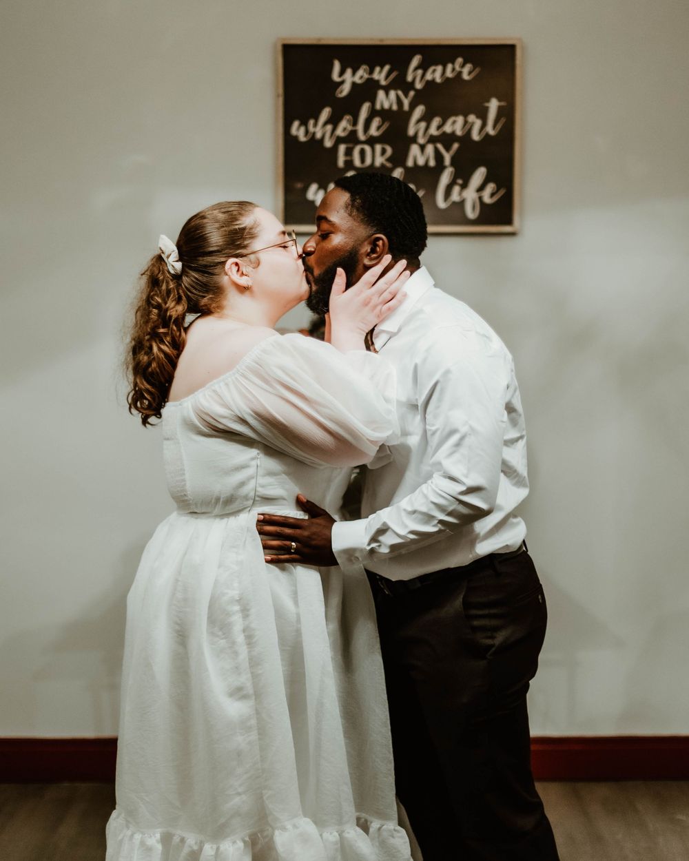 A romantic courthouse wedding scene shows a couple embracing in front of decorative wall art.