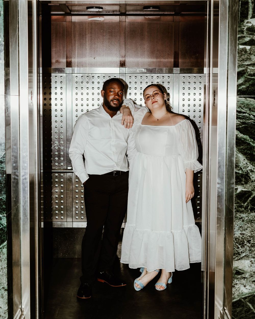 Couple sharing joyful moments in modern elevator with metallic interior design.