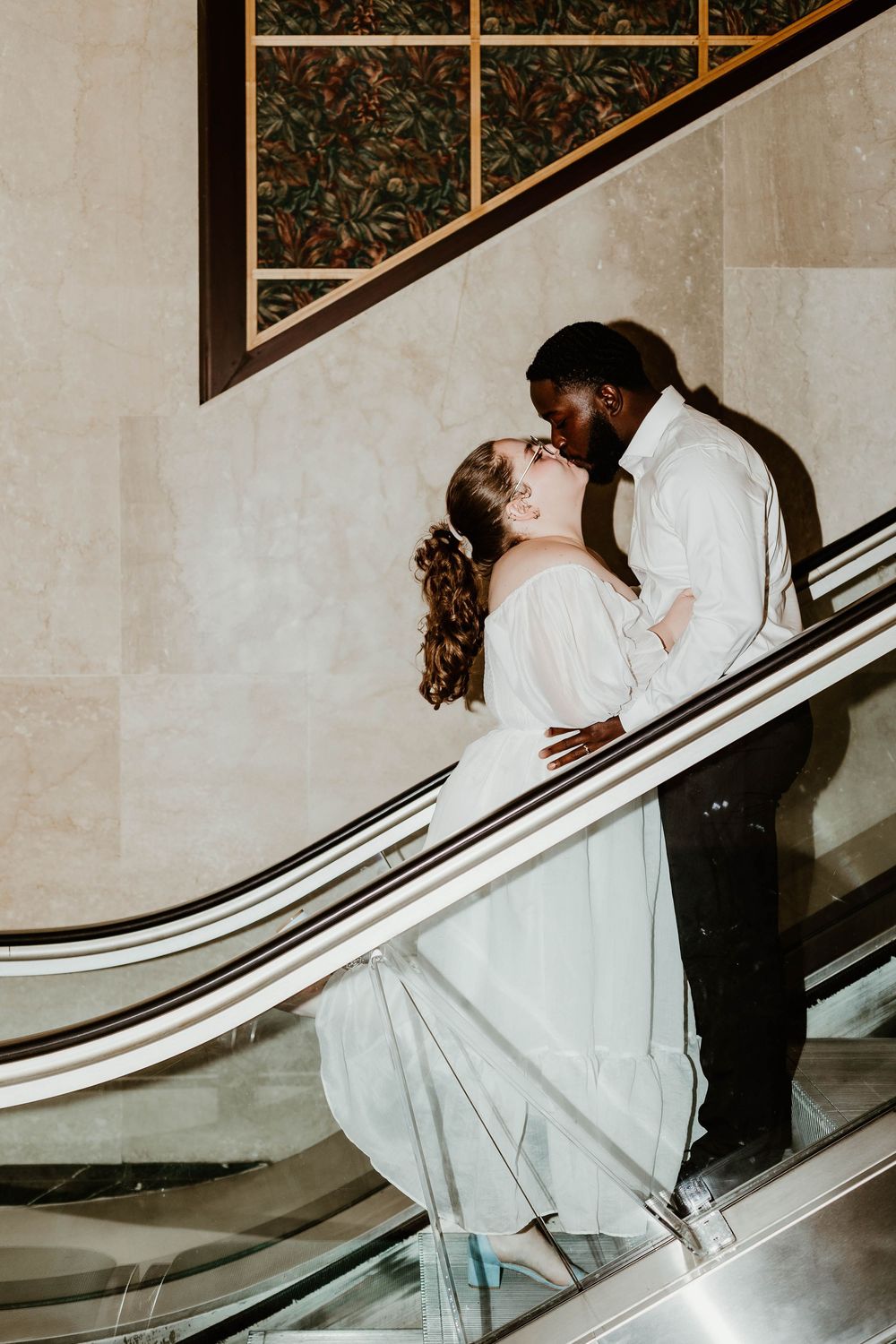 A couple creates a romantic moment on an escalator in an elegant building interior.