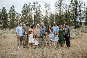 Extended family photo session in a rustic field with pine trees in the background.