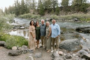 Family photos taken along a rocky riverbank with flowing water and evergreen trees.
