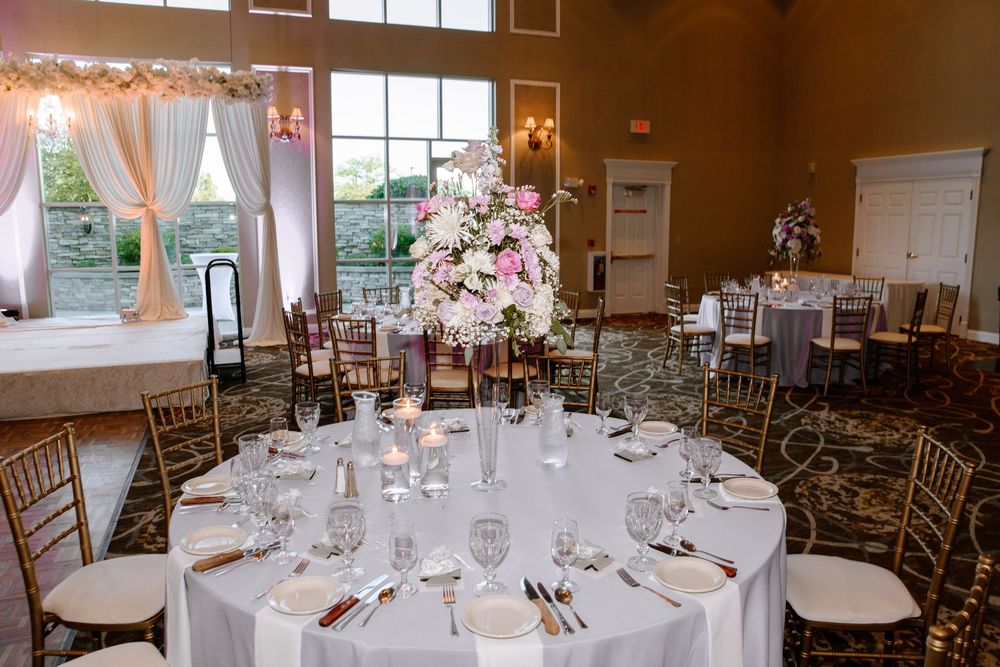Elegant round tables with white linens and floral centerpieces set up in a formal dining room for a wedding reception.