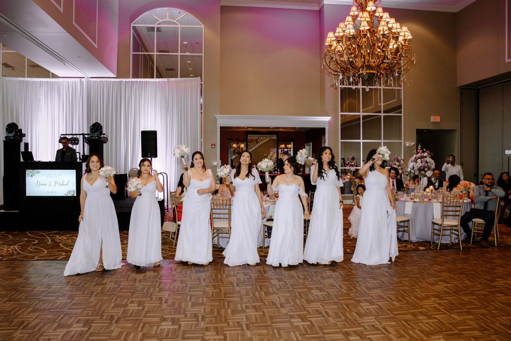 Reception hall set for dinner with white chairs, chandelier lighting, and elegant decor arranged around the room.